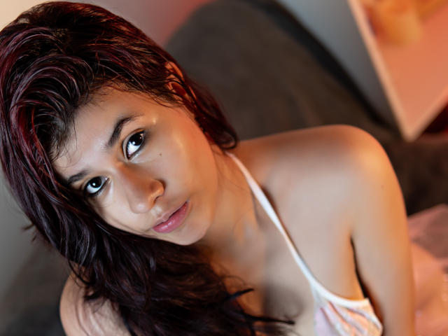 MillaCasanova with wet dark red hair, gazing up, wearing a white halter top, showing her bare shoulders and small, perky tits. Her brown eyes and pink lips stand out.