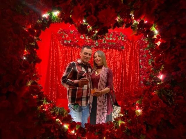 LucianSins with red roses, wearing a plaid shirt and jeans, stands next to LucianSins with a striped top, holding an orange object, surrounded by a heart-shaped red rose frame.