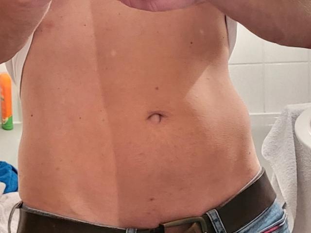 Het kale, gespierde torso van HarteLatte, met een zichtbare navel, lichte huid, lichte spierdefinitie, gekleed in blauwe jeans met een zwarte riem, en witte onderbroek die gedeeltelijk zichtbaar is..