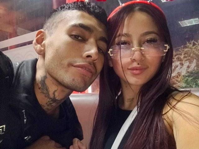 LoveBirds69, with dark hair and tattoo, leans on LoveBirds69, who has long red hair, glasses, and a nose ring, showing off a cute smile. Both have sexy looks.