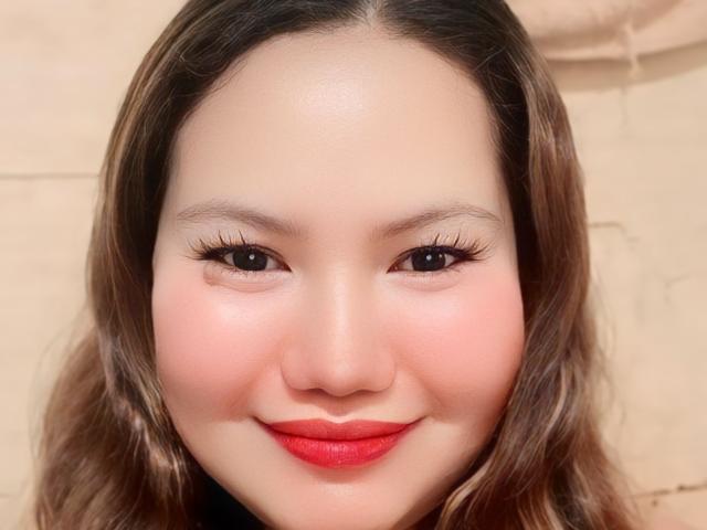 VoluptuousLady has a cute face with pinkish cheeks, red lipstick, and long eyelashes, looking directly at the camera with a slight smile. Her brown hair is wavy.