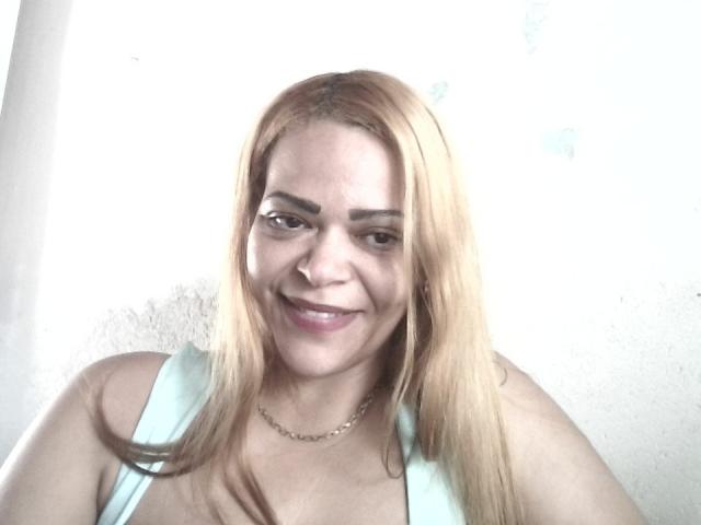 DeborahSweetX has blonde hair, a cute smile, and light skin, wearing a light blue top with a gold chain necklace, showing her small tits.