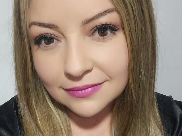 Il viso di NatalyHami, con i capelli biondi, gli occhi marroni e il rossetto rosa, indossa una maglietta nera, ha un leggero sorriso e le ciglia sono visibili. Il suo seno non è visibile..