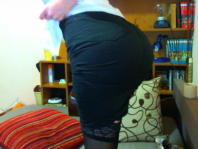 ChatePoilue's ass in a tight black skirt, showing lace top thigh stockings, with white shirt, standing in a room, focusing on her butt and skirt.