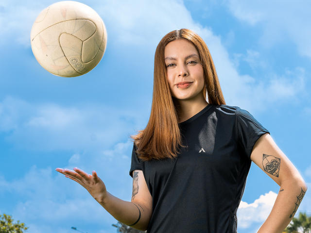 VictoriaOrtega with straight red hair, black sports tee, tattoos on arms, smiling, ball mid-air, right hand out, blue sky background. She's got a cute ass and medium tits.