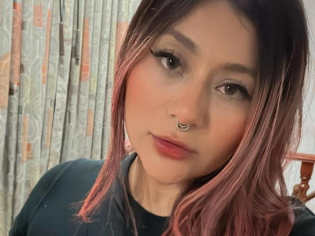 LorraineV with pink ombre hair, black eyeliner, nose ring, and pink lips, wearing a black top, looking at the camera with a slight smile.