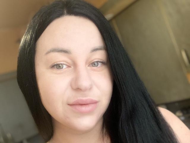 VeronikX heeft recht zwart haar, bleke huid, groene ogen en roze lippen. Ze kijkt naar de camera met een lichte glimlach. Haar borsten zijn niet zichtbaar..