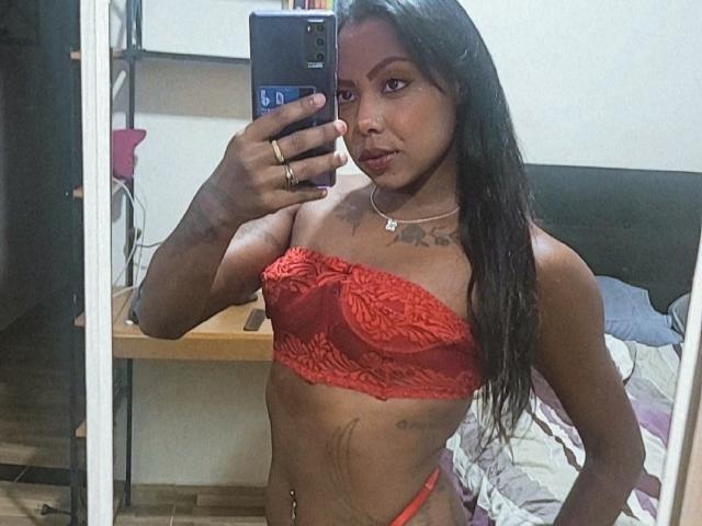 KarenEbony with dark skin, long black hair, red lace bra, and red thong, holding phone, showing small tits, tattoo on chest, belly button piercing, mirror selfie.