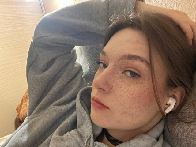 LateNightX heeft een huid met sproeten en een bleke teint, met lichtbruin haar, draagt een grijze hoodie, ligt plat met oordopjes in, met een hand op zijn hoofd, heeft groene ogen en een ontspannen, lichtjes fronsende uitdrukking..
