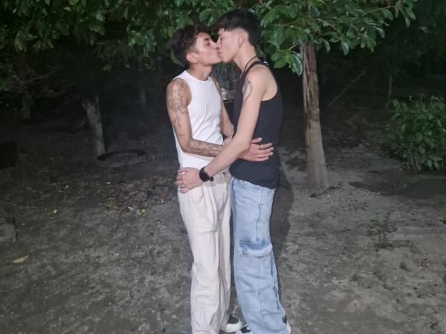 TaylorAndChris kissing, TaylorAndChris with tattoos, wearing white tank top and pants, black tank top, blue jeans, standing, arms around each other, night, tree in background.