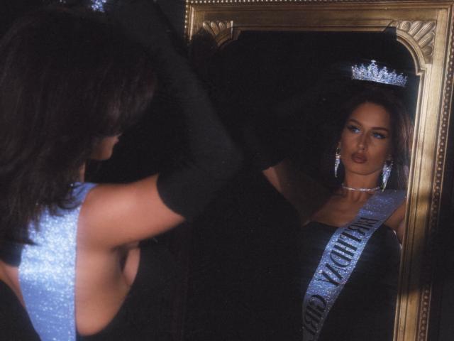 LanaXStorm with shiny blue crown, black dress, and silver sash, looking at mirror reflection, black elbow gloves, silver earrings, and serious expression, dark hair, elegant, reflective.