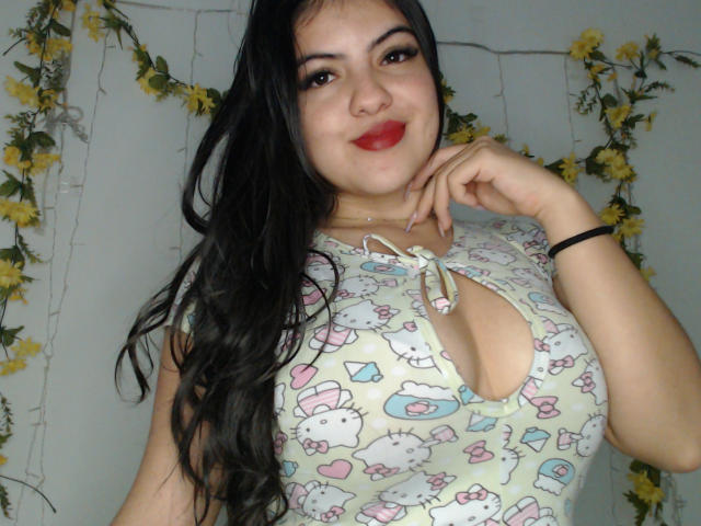 AlissonS has long black hair, red lipstick, and a cute smile, wearing a white Hello Kitty top with a keyhole cutout showing her big, perky tits.