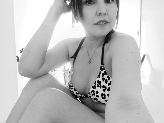 AdelaShery con un sujetador de estampado de leopardo, senos medianos, sentada con la rodilla levantada, brazo levantado, selfie en blanco y negro, collar, sonrisa sutil, cabello oscuro, piel clara, informal, segura de sí misma..