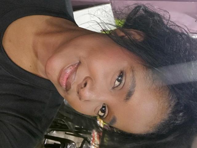 Fer69s has dark brown skin, shiny pink lips, and black curly hair. Fer69s is wearing a black shirt, looking up with brown eyes. Fer69s' face is centered.