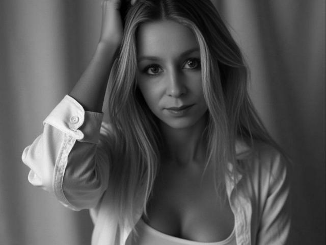 Schwarz-weißes Foto von Dina Richards mit langen blonden Haaren, die ein offenes Hemd trägt, wobei ihre Brüste sichtbar sind. Sie blickt verführerisch in die Kamera, eine Hand in ihrem Haar..