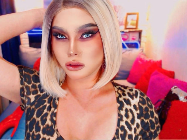 QueenNhicolle-hot with blonde bob, blue eyes, and dark makeup, wearing a leopard print top, has her hand in her hair, showing off her tits and red lips.