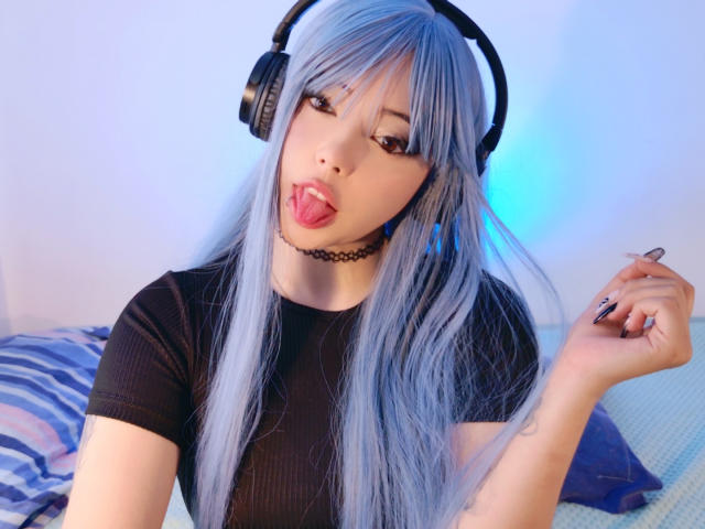 Arieyaara, avec des cheveux bleus, un casque noir, un collier noir, une chemise noire, la langue tirée, tenant une bague, peau pâle, regardant la caméra, mignonne, espiègle, sexy..