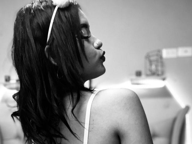 Black and white photo of LolitaRose with wet dark hair, wearing a white headband and bra, eyes closed, lips slightly parted, showing her shoulder and profile.
