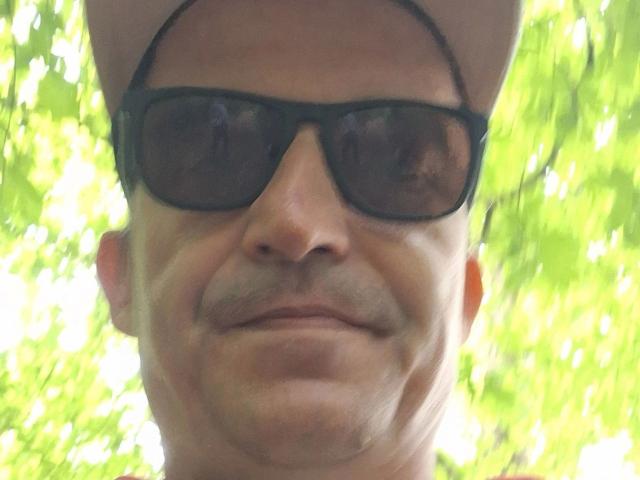 Tom Stern, mit schwarzen Sonnenbrillen und einem kaum merklichen Grinsen, trägt eine hellbraune Mütze und hat deutliche Gesichtsfalten. Seine Nase und sein Kinn sind markant..