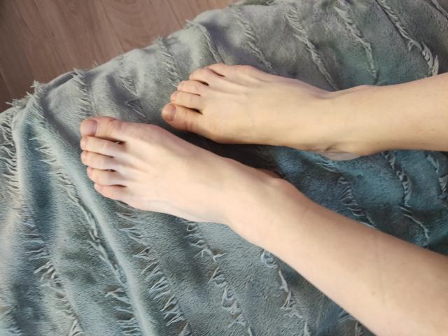 EvaMcCoy's feet are resting on a fringed, blue-gray fabric. Her toes are slightly curled, and her pale skin contrasts with the textured material.