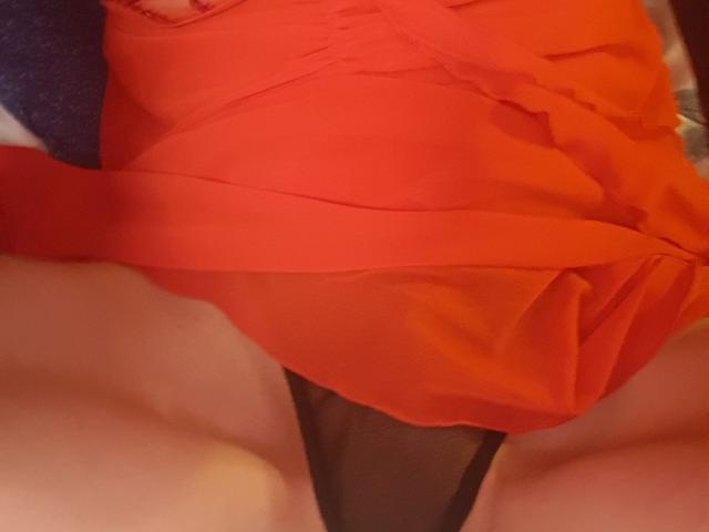 MalenaLoveSex's red dress is pulled up, revealing black panties and her bare thighs. Her pale skin is visible. The dress is ruffled and sits above her pussy.