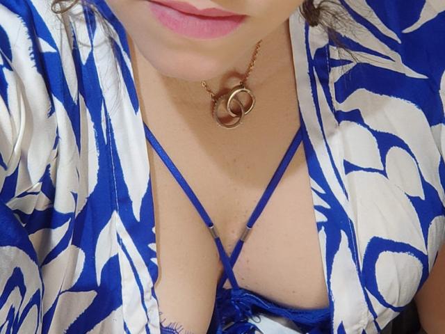 ChubbyAngel69's tits, covered in a blue and white patterned dress, showing a blue strappy bra, with a gold necklace featuring intertwined circles, and pink lipstick.