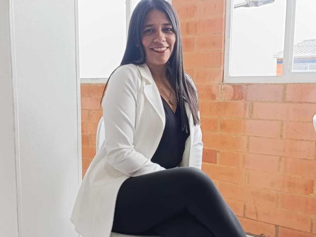 PauletteLoveX has long black hair, a cute smile, and is wearing a white blazer over a black top with black pants, sitting with her legs crossed.