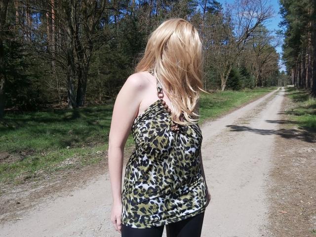 Mandy4you-hot with blonde hair, wearing a leopard print halter top, standing on a dirt road, facing away, showing her ass in black pants.