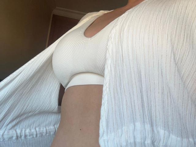 AlexaRoro-hot's white ribbed shirt is open, revealing her small, firm boobs in a tight white top. Her right arm is visible, and the shirt's texture is ribbed.