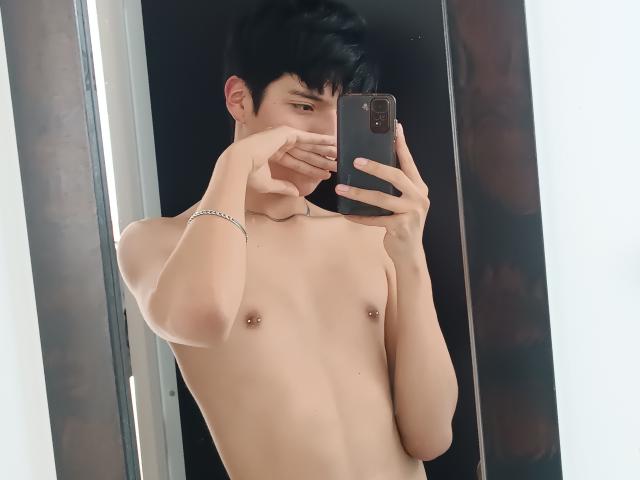 CallMeSugar, shirtless, with small pierced nipples, black hair, holding a phone, covering his face, wearing a silver bracelet, taking a mirror selfie.