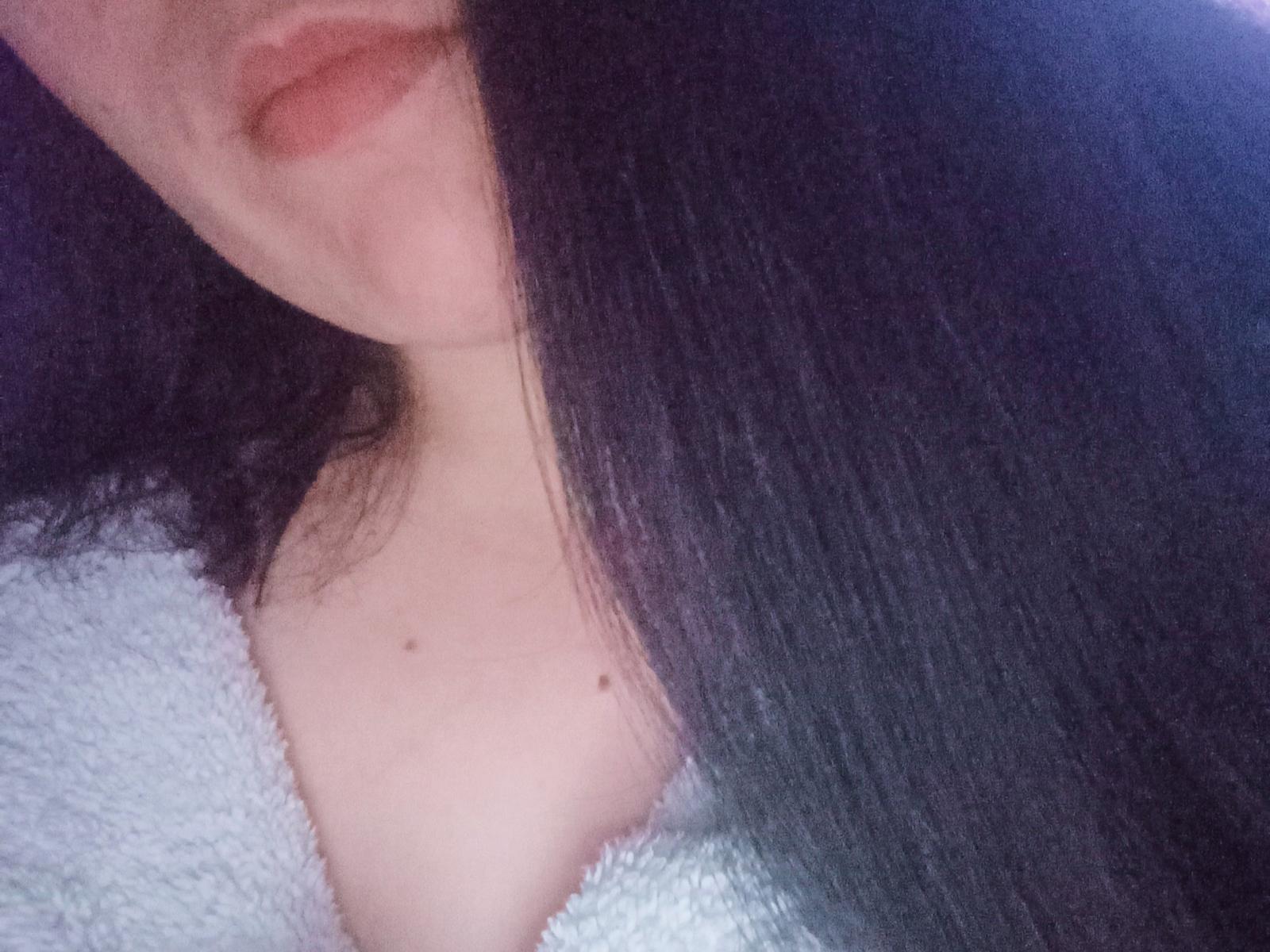 AlikaSun's face with long black hair, slightly parted lips, and a small mole on her chest, wearing a fluffy white robe, showing a bit of her tits.