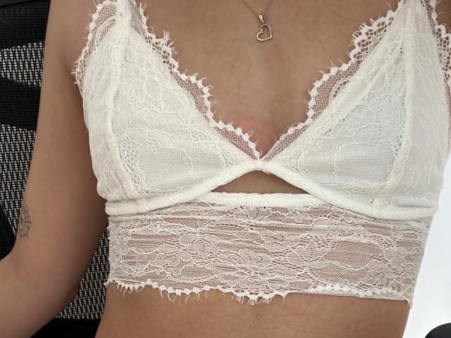 AngelEmma69's white lace bralette, featuring a deep V-neck and cut-out section under the bust, showcasing her small tits and a delicate necklace with a small pendant.