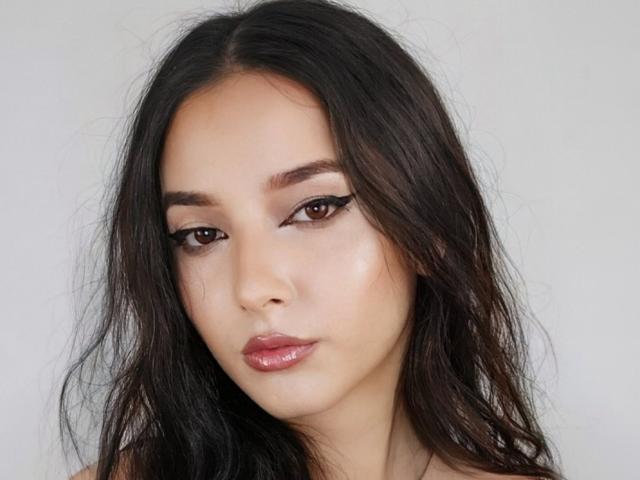 AngelEmma69 heeft lang, donker, lichtelijk rommelig haar, bruine ogen met dikke zwarte eyeliner en glanzende, roze-rode lippen. Haar huid is glad en licht. Ze ziet er serieus uit..