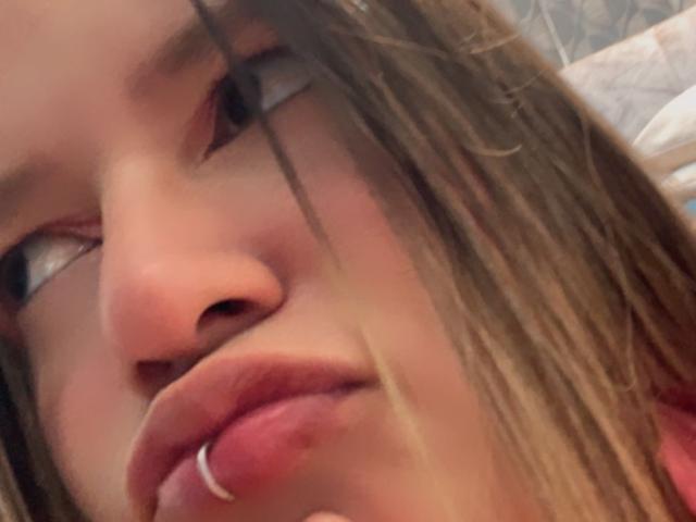 AliceHoe's face with a nose ring, light brown hair, and pink lips, slightly parted, showing soft skin and a subtle smile. Her eyes look to the side.