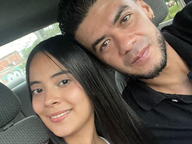 TamaraAndy's face is next to a man's face in a car, both smiling. TamaraAndy has black hair, brown eyes, and is wearing pink lipstick. The man has a beard.