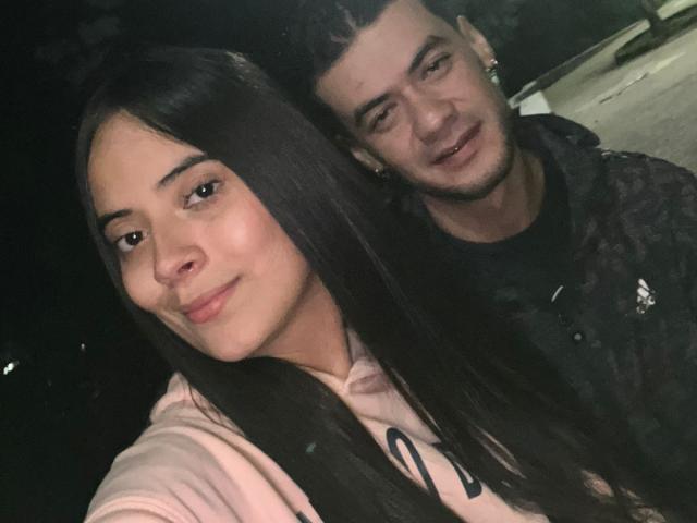 TamaraAndy with long black hair, light skin, and pink hoodie, stands next to a guy with short black hair, black shirt, and slight smile. Both have cute, relaxed expressions.