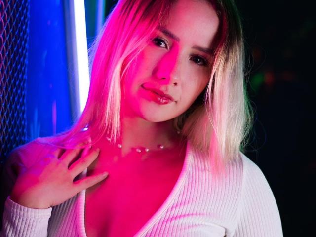NatSorian met blond haar, roze en blauwe neonlichten, wit geribbeld shirt, hand op de borst, subtiele glimlach, glanzende roze lippen, ketting, zacht licht op het gezicht, sexy, schattig..