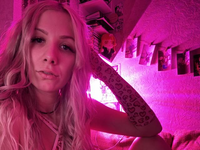 LapinaAnna, con i capelli rosa, guarda la fotocamera, indossando una manica a stampa leopardo, una collana rosa e un trucco leggero, con un'illuminazione rosa. Il seno non è visibile..