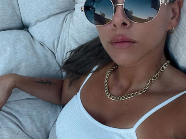 SexOnMyLeVeL: una ragazza attraente sdraiata su un divano, indossa una canotta bianca, una catena d'oro e occhiali da sole aviator riflettenti, ha un tatuaggio sul braccio e il sedere è parzialmente visibile..