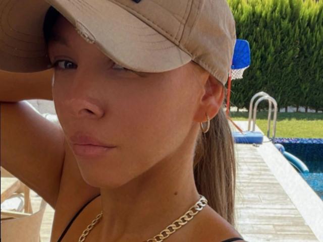 SexOnMyLeVeL – eine Frau mit gebräunter Haut, braunen Augen und einer flachen Nase, trägt eine beige Mütze, eine goldene Kette und goldene Ohrringe und zeigt ein ernstes Gesicht am Pool..