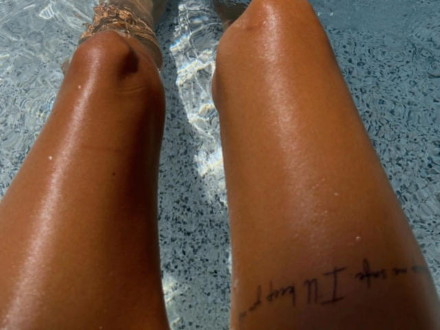 Los muslos bronceados y húmedos de SexOnMyLeVeL-hot brillan en una piscina, con un tatuaje en el muslo derecho que dice "Hago lo que quiero" en tinta negra..