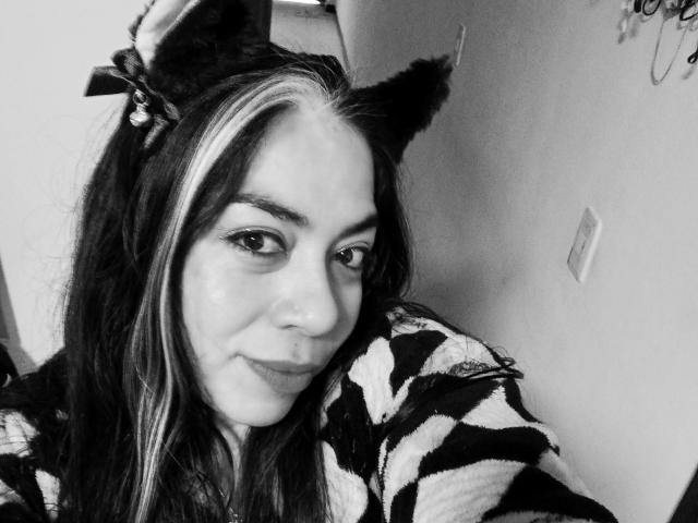 Black-and-white selfie of EvaLunaLatina with cat ears, long dark and light-streaked hair, and zebra-patterned top, smiling slightly, showing her cute face and small nose.