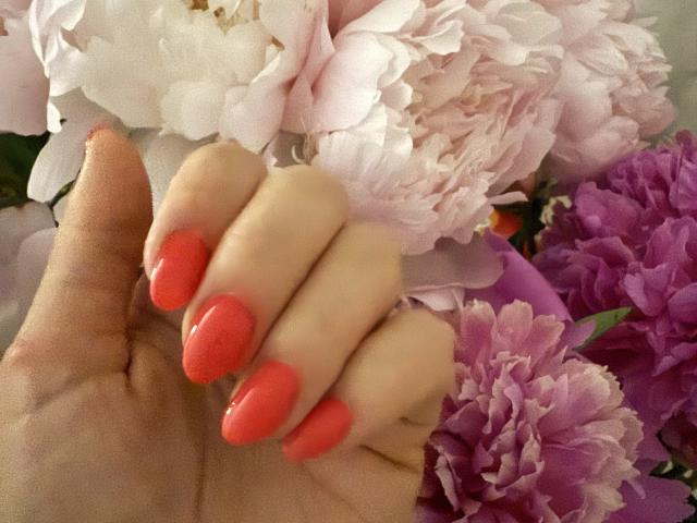 Stefanni's hand with bright red, glossy nails resting on pink and purple flowers. Her fingers are slightly curled, showing off her shiny, well-manicured nails.