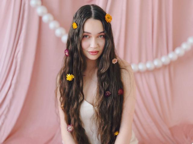 LilianCat-hot with long, wavy brown hair, yellow and red flowers in it, wearing a white dress, pink backdrop, smiling, soft light, cute, feminine, attractive, sexy.