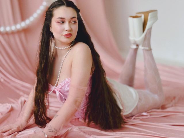 LilianCat-hot with long brown hair, pink eyelids, pearl necklace, pink corset, white heels, and pink stockings, lying on pink satin, showing her tits and ass.