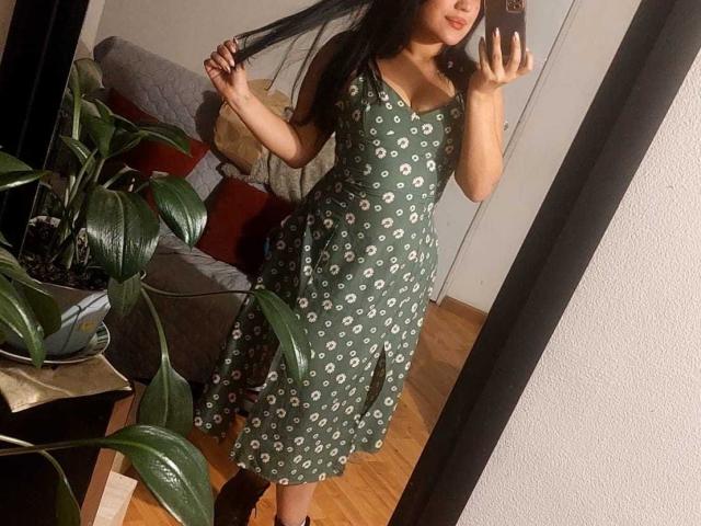 LauraRichis with long black hair, wearing a green dress with white and gray patterns, holding her hair, standing in front of a mirror, showing her tits and ass.