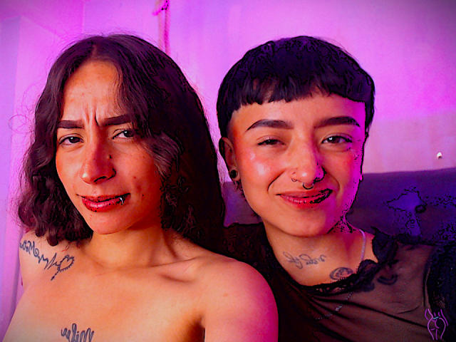 Riley e Alexa, senza indumenti superiori, con tatuaggi, che mostrano la lingua e con piercing metallici al naso, illuminate da una luce rosa-viola. Riley ha i capelli ricci, Alexa ha i capelli corti, entrambe hanno un anello al naso..