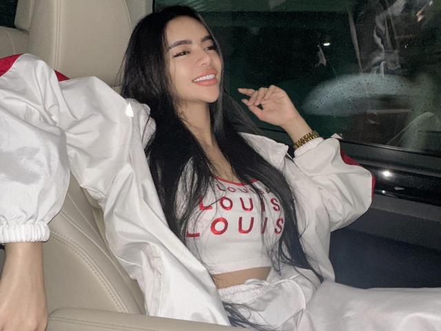 EvaPapaya with long black hair, smiling, wearing a white jacket and gray crop top, showing her tits, sitting in a car at night, holding a cigarette.
