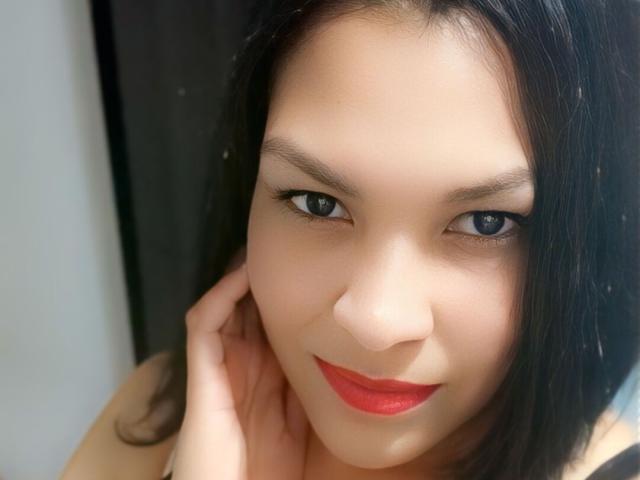 HazanFoxy a la peau claire, les cheveux noirs, les yeux bleus et porte du rouge à lèvres. Une de ses mains touche sa joue, et elle regarde directement l'appareil photo. Ses seins ne sont pas visibles..