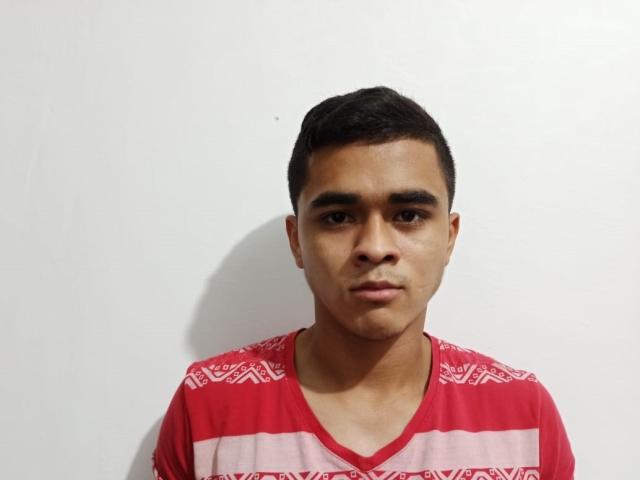 RandyPein, un ragazzo con i capelli castano corti e la pelle media, indossa una camicia a righe rosse e rosa, ha un'espressione seria, e c'è una piccola ombra su un muro bianco..